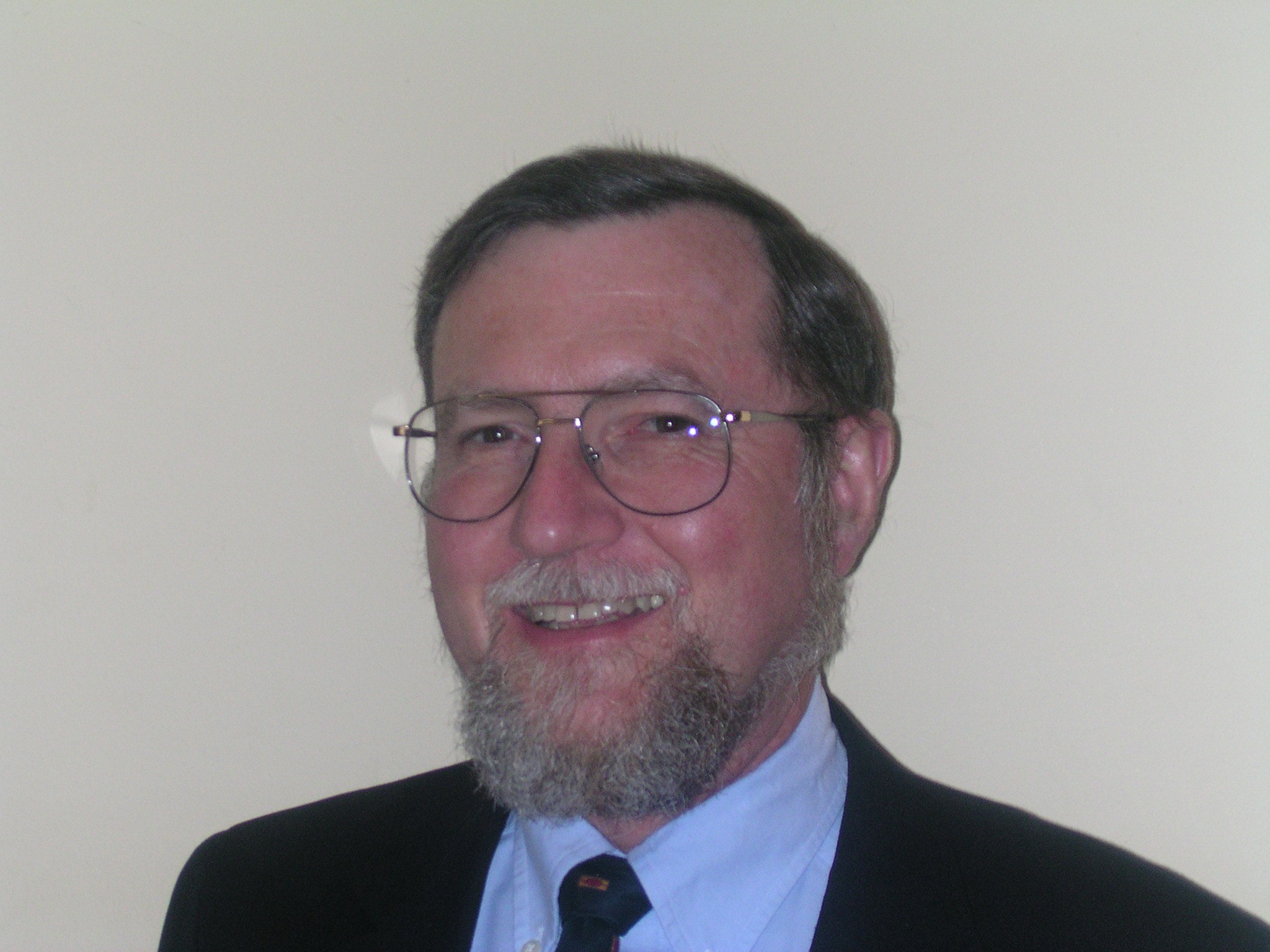A photo showing Ian Greene. Ian wears spectacles and has brown hair with a grey beard. He is dressed in a black suit.