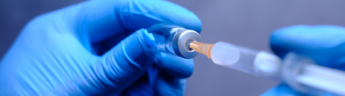 An individual wearing blue medical gloves holding a vaccine